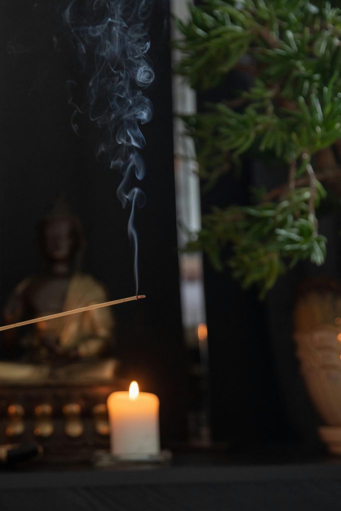 Serene meditation setup with incense smoke, candlelight, and Buddha statue.